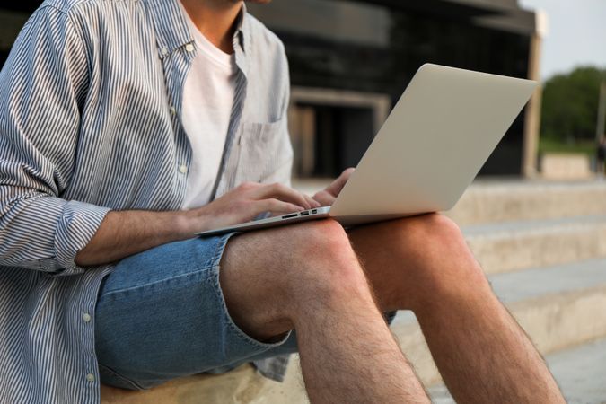 Young man sits in steps and working in laptop outdoor. Freelancer