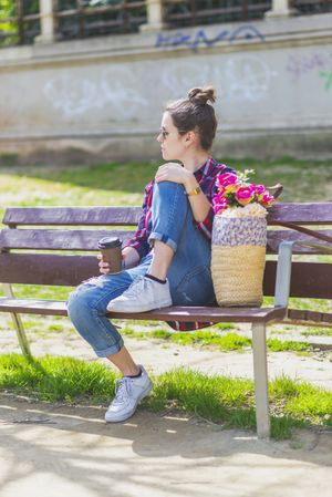 Side view of a young hipster woman sitting on a park bench relaxing in a sunny day while looking away