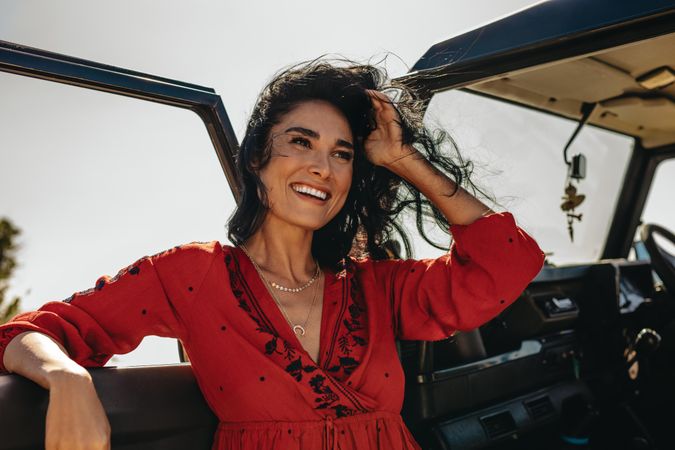 Happy young woman standing near her car with wind blowing her hair