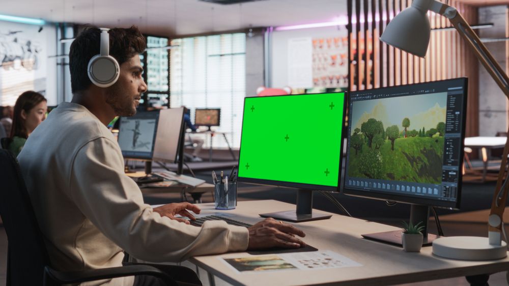 Indian Male Game Designer Using Desktop Computer With Green Screen Chromakey on Display, Designing Immersive World In 3D modelling Software For RPG Video Game.