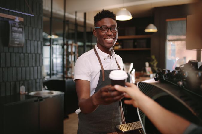 Man handing customer a coffee while smiling at a coffee shop