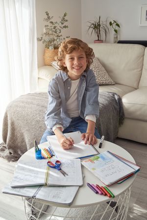 Cheerful preteen boy drawing on paper at home