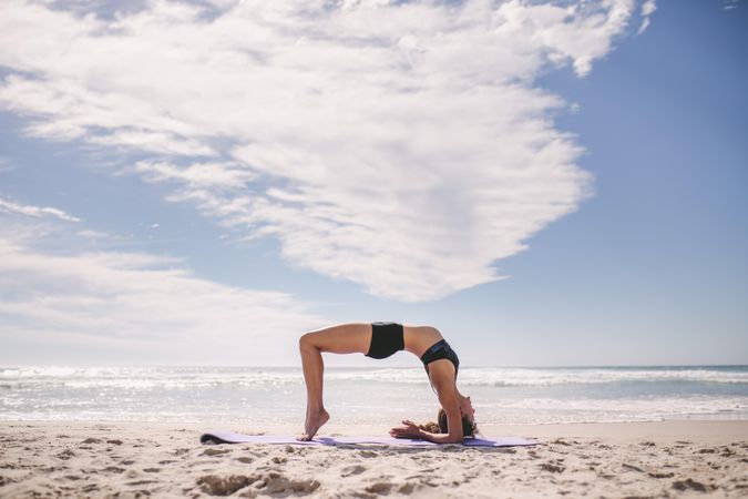 Flexible woman doing back bend at the beach