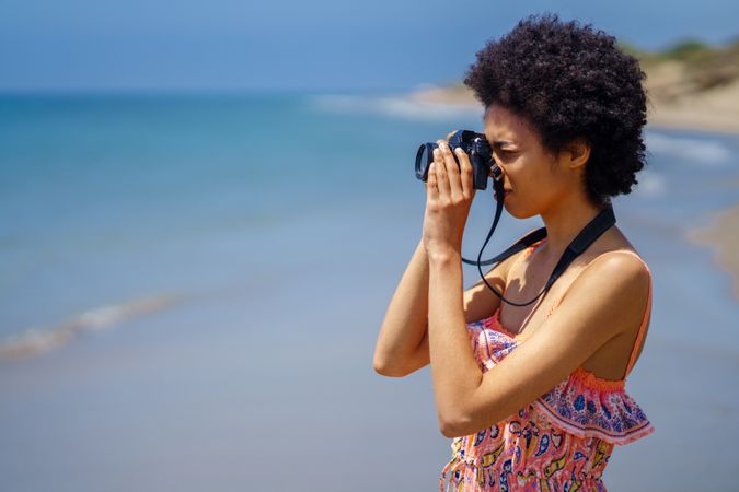 Woman with camera to her face as she takes pictures of beautiful beach