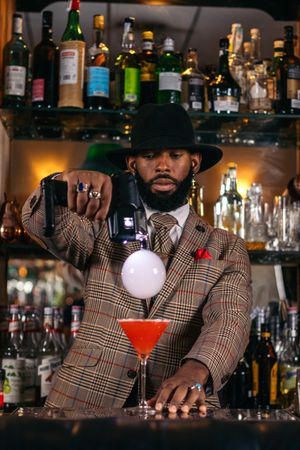 Stylish Black bartender preparing a cocktail with a smoke bubble in a traditional cocktail bar