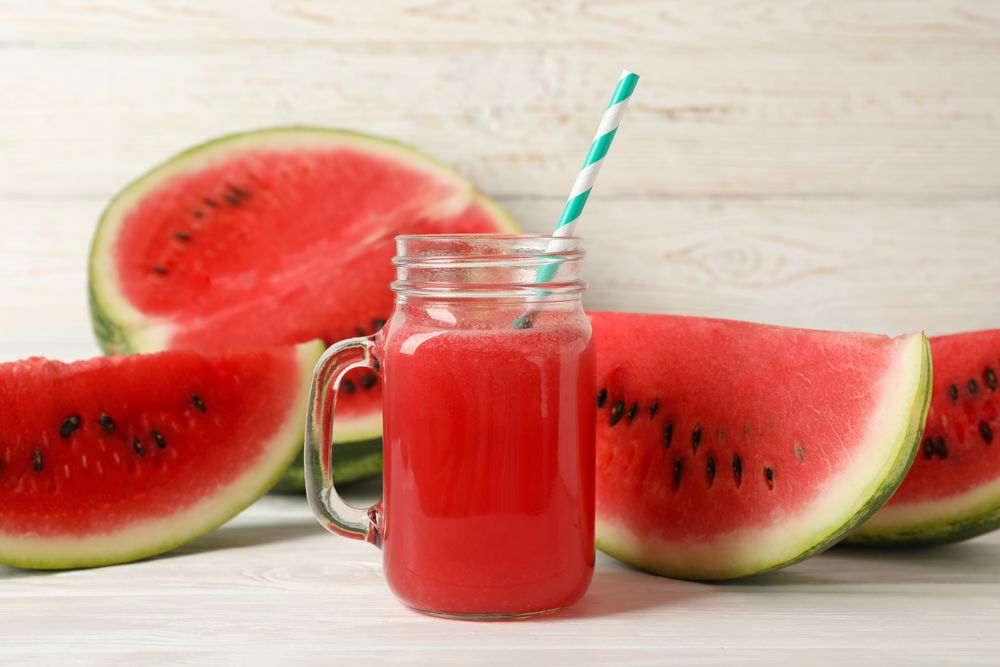 Glass jar of watermelon juice and slices on wooden background