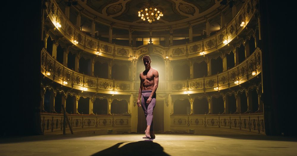 Cinematic Shot of Male Ballet Dancer Standing on Classic Theatre Stage with Dramatic Lighting and Looking at Camera.