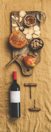 Cheese plate with bottle of red wine on light brown linen, vertical composition