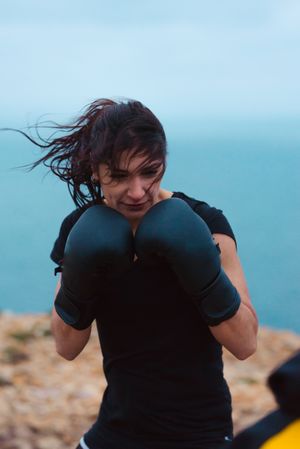 Woman Kickboxer training on cliff near sea