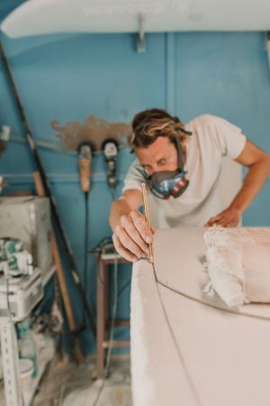 Man in respirator measuring surf board in workshop