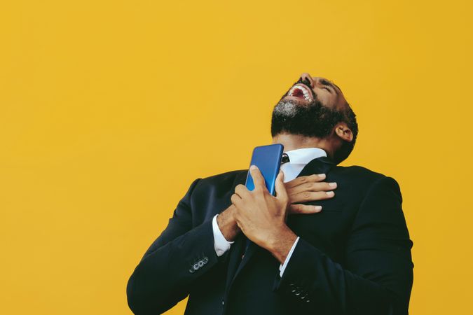 Animated Black businessman in suit laughing with hand to his chest while looking at smartphone