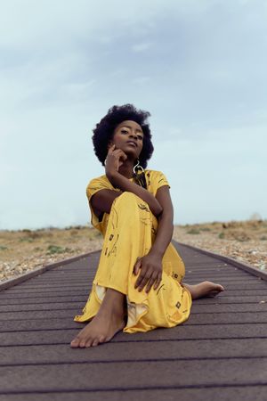 Woman in yellow dress sitting on wooden pathway in desert