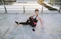 Woman with earphones and smartphone stretching on embankment