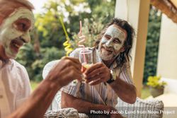 Happy older people toasting juice glasses with facial clay mask on 5kjjj0