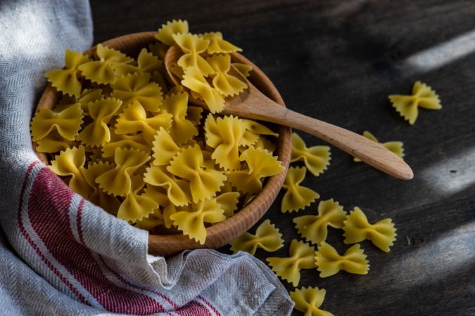 Farfalle pasta in wooden bowl on kitchen counter with kitchen towel