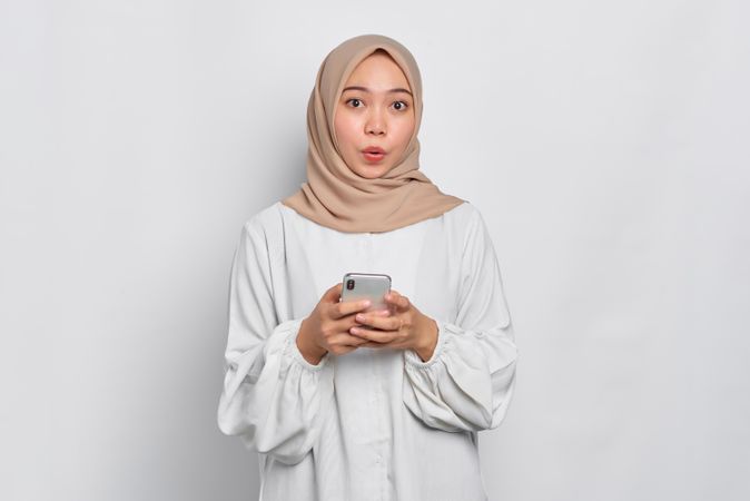 Asian female in headscarf receiving surprising news on her cell phone