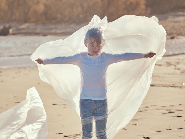 Calm boy rolled in plastic film with stretched hands aside