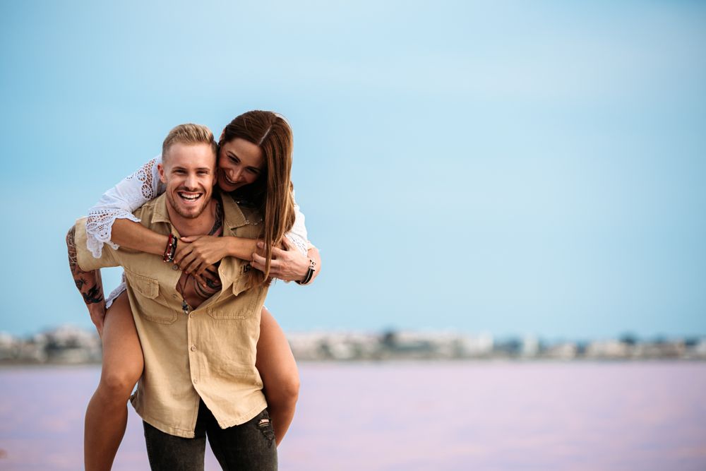 adorable couple giving a piggyback ride on an amazing beach of pink water