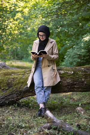 Middle Eastern woman leaning on tree while reading