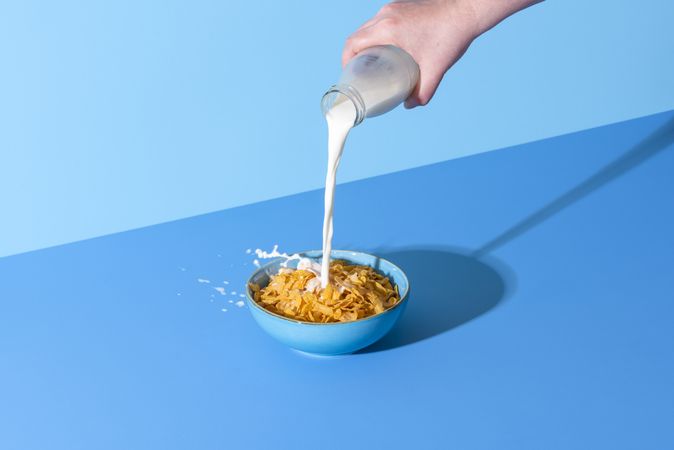Pouring milk in a cereal bowl on a blue background