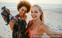 Two young women holding garbage bags and taking selfie at the beach area 0yqpn0