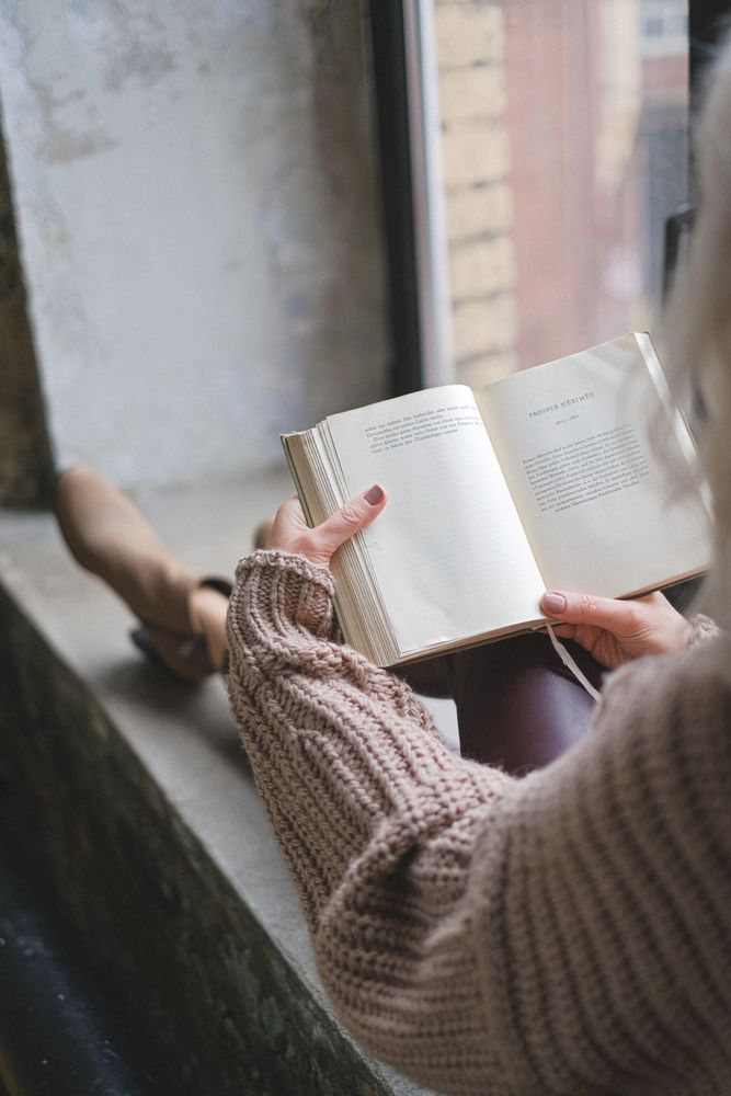 Back view of person sitting by window and reading a book