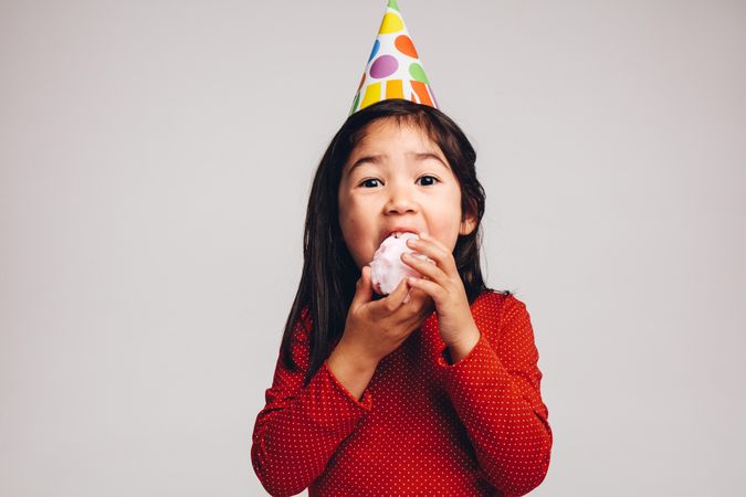 Excited young girl wearing a birthday party hat and eating candy