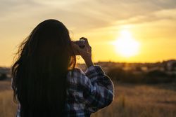 Young woman taking photos with analog camera in the field at sunset