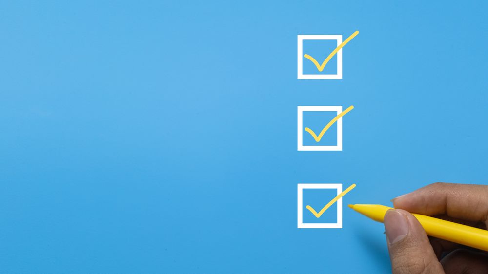 close up of male hand holding yellow marker and checklist three checkbox isolated on blue background