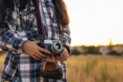Unrecognizable woman taking photos with analog camera at sunset