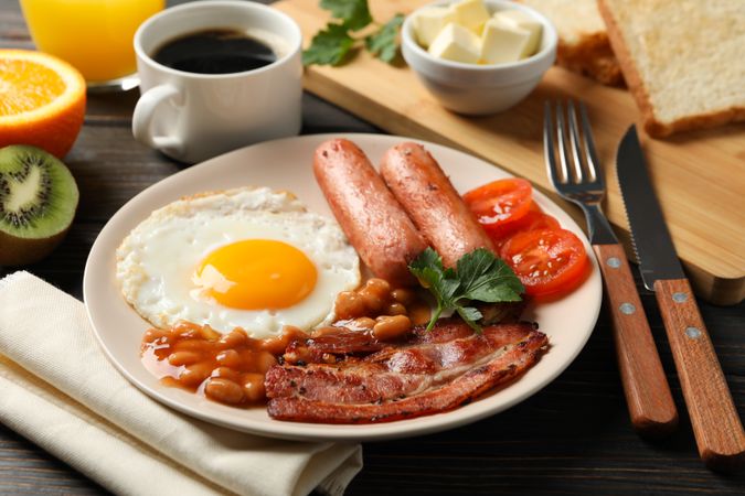 Two fried eggs sunny side up on plate with bacon, sausage, and coffee