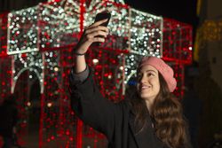 Happy young woman in cap standing and taking selfie with smartphone