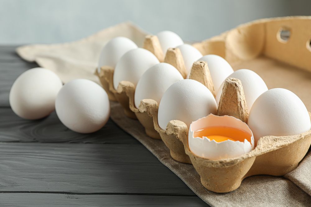 chicken eggs in carton box on wooden table, space for text