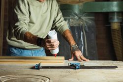 Crop carpenter gluing wooden board in workshop