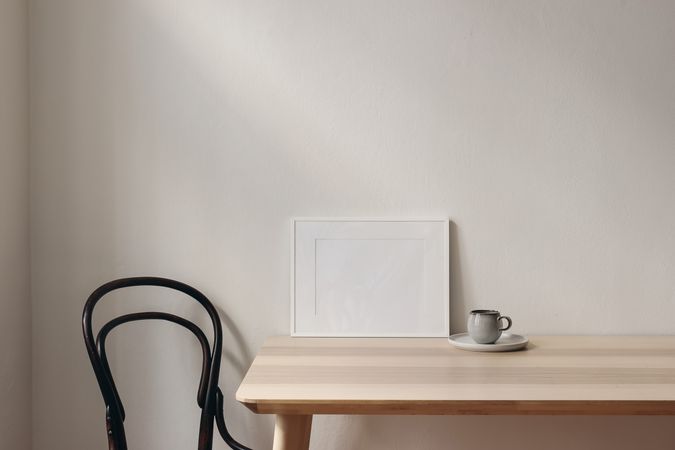 Picture frame mockups on wooden table. Cup of coffee, vintage chair. Scandinavian interior, neutral color palette. Artistic display concept, no people. Copy space