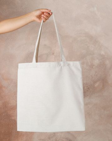 Female hand holding tote bag against brown background, empty space