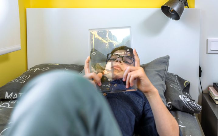Relaxed boy watching video in a futuristic transparent tablet laying over his bed