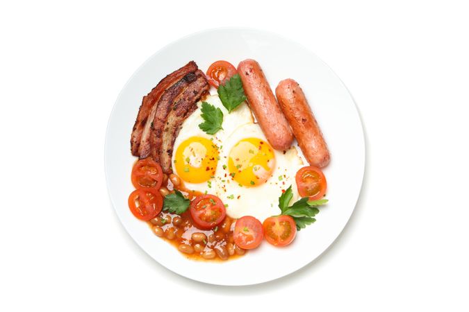 Top view of breakfast plate with fried eggs, sausage, bacon, beans and tomatoes