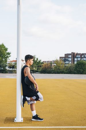 Young man leaning on basket on basketball court outdoor.