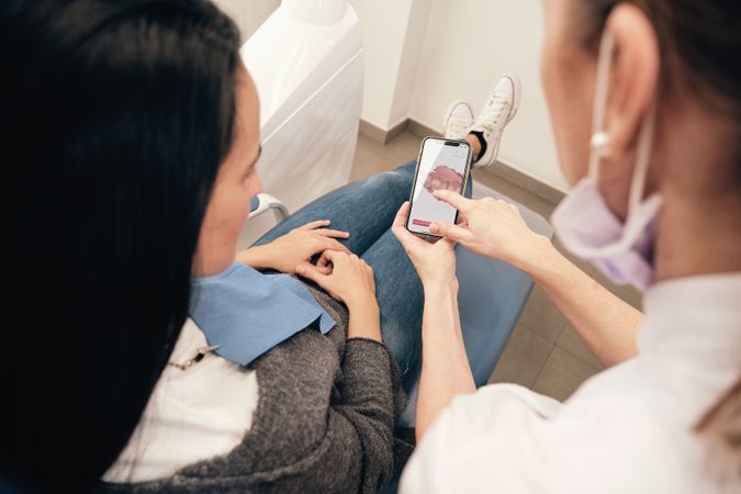 Crop orthodontist showing teeth scan on smartphone to female patient