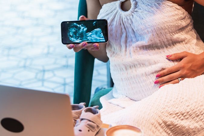 Anonymous Black pregnant woman showing baby ultrasound picture to laptop