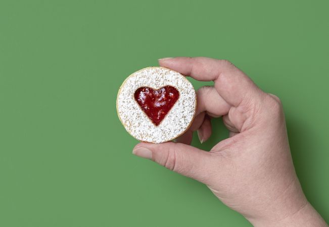 Linzer cookie in woman hand on a green background, above view
