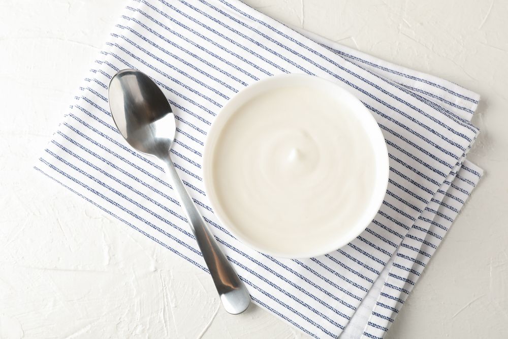 Bowl of sour cream yogurt, spoon and towel on cement background