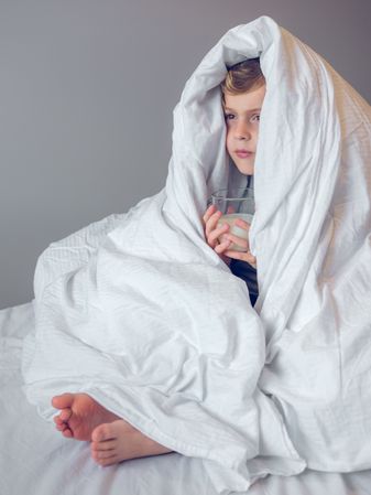 Little boy wrapped in blanket on bed
