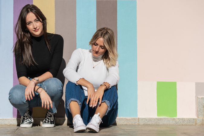 Happy girlfriends sitting against painted urban wall