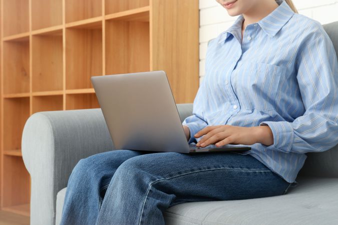 Young woman with laptop sitting on sofa in modern flat