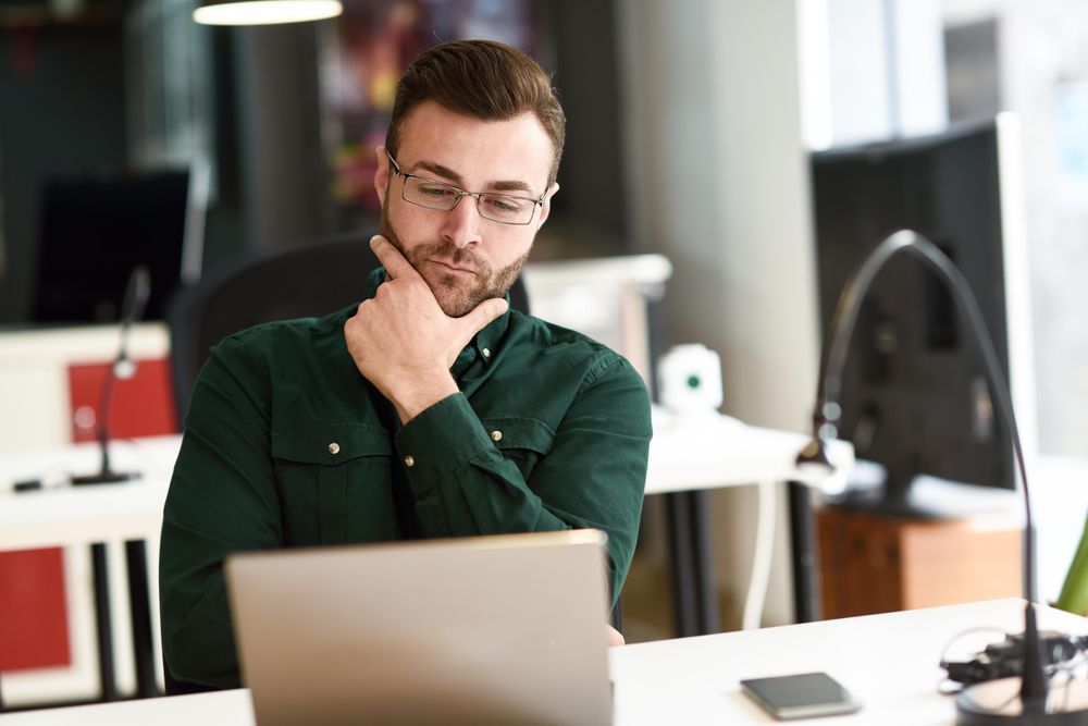 Young man reading his computer screen in modern office