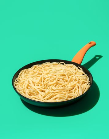 Spaghetti in an iron cast pan isolated on a green background