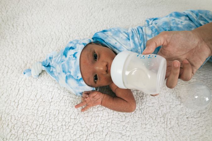 Anonymous mother feeding newborn baby wrapped on soft blanket