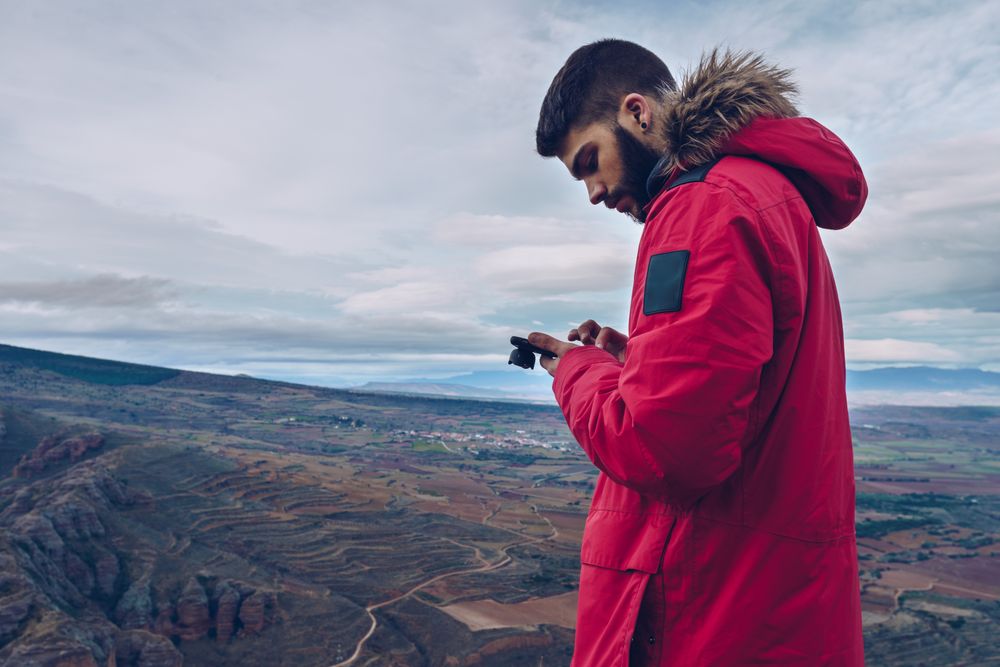 Focused tourist browsing smartphone while standing at mountain top